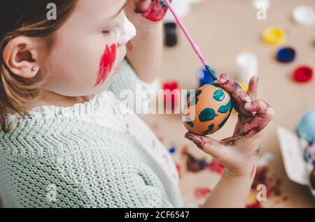 girl with brush coloring chicken eggs at table in room Stock Photo
