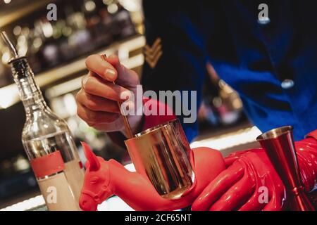 unrecognizable barman in uniform and red gloves preparing cocktail for mixing Stock Photo