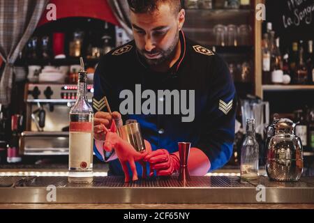 unrecognizable barman in uniform and red gloves preparing cocktail for mixing Stock Photo