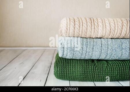 stack of knitted warm sweaters in pastel colors on light wooden table in the room Stock Photo