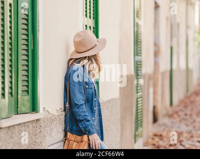 Side view of young smiling Woman leaning on stone building outside with green windows Stock Photo