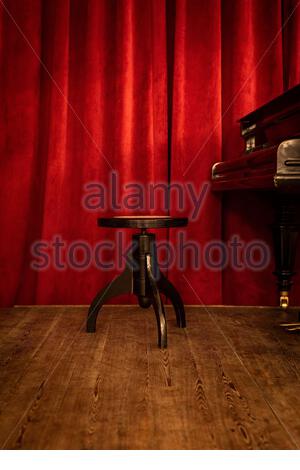 A piano bench on stage on red curtain background. Stock Photo