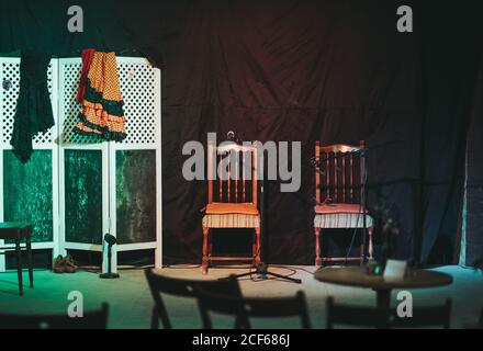 Empty theater platform with wooden chairs and flamenco dresses put on portable partition and with pair of shoes and standing microphones on floor Stock Photo