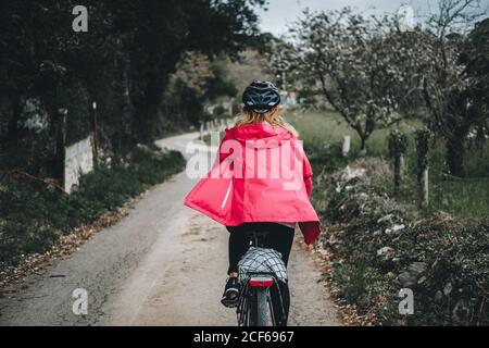 Back view of anonymous woman while cycling on countryside road on cloudy day