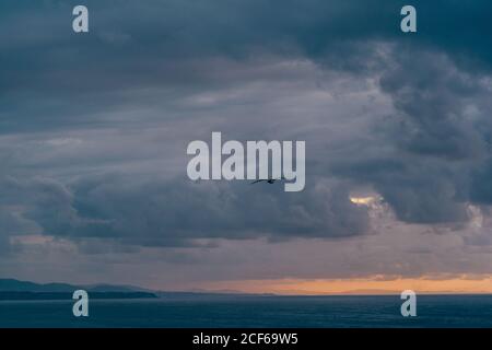 Dark gray clouds swirling on stormy sunset sky over rippling sea in evening in nature Stock Photo