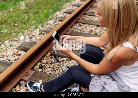 Cheerful Woman sitting on railway with smartphone Stock Photo