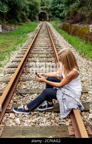 Cheerful Woman sitting on railway with smartphone Stock Photo