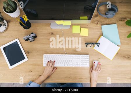 Top view of anonymous cropped caucasian Woman sitting on wooden desk working on a computer in a modern home office Stock Photo
