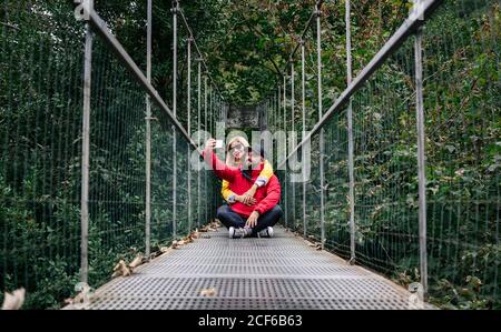 Cheerful couple of tourists taking selfie on bridge in summer Stock Photo