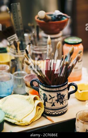 From above of table with cans with colors and paint brushes located around white ceramic cup with blue patterns and brushes inside Stock Photo