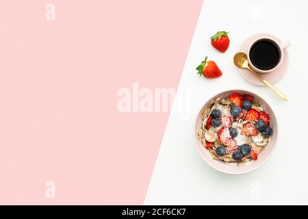 Top view of breakfast bowl with yummy muesli and berries placed on table with cup of coffee and fresh strawberries Stock Photo