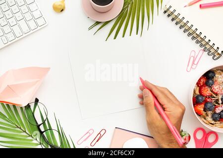 Top view of anonymous male with blank sheet of paper and pen sitting at white table with breakfast bowl and cup of espresso Stock Photo