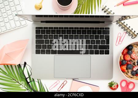 From above of netbook placed on white office desk and surrounded by fresh breakfast bowl and cup of aromatic coffee Stock Photo