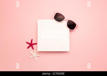Top view composition with sunglasses and colorful starfish arranged near blank paper sheet copy paste on pink background Stock Photo