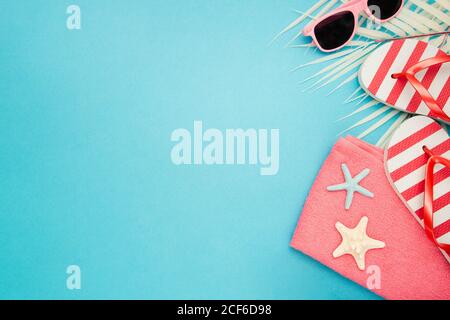 Top view composition of sunglasses and flip flops placed with beach towel on blue background with palm leaves and starfish representing summer vacation on beach Stock Photo