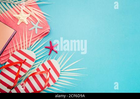 Top view composition of flip flops placed with beach towel and notebook on blue background with palm leaves and starfish representing summer vacation on beach Stock Photo