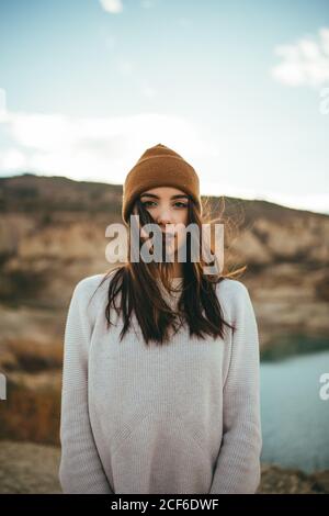 Youthful charming female tourist looking at camera while enjoying weekend journey to lake in autumn Stock Photo