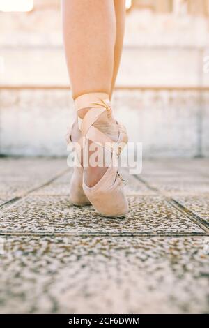 Crop female dancer wearing pointe shoes standing on tiptoes on weathered stone ground and demonstrating dancing position Stock Photo