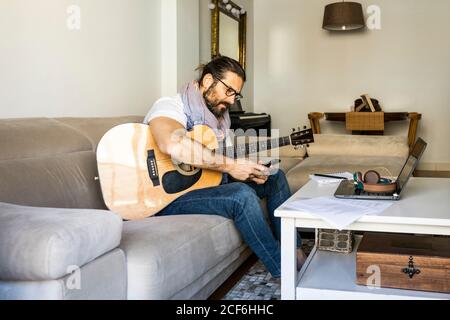 Cheerful man with guitar checking smartphone on sofa Stock Photo