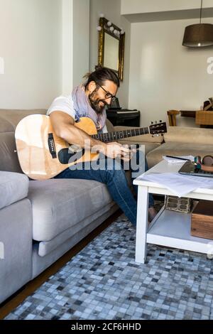 Cheerful man with guitar checking smartphone on sofa Stock Photo