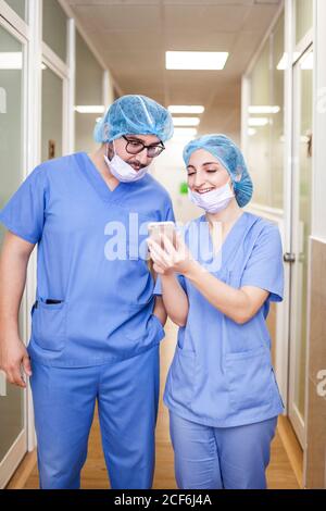 fellow surgeons man and Woman chat while walking to the operating room, she shows her smartphone to him and smiling Stock Photo