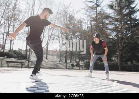 man looking at young dancer in casual wear doing handstand in park in sunny weather Stock Photo