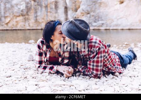 Side view of young couple lying and kissing on rock coast of mountain river near cliff Stock Photo