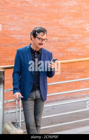 Aged man standing with baggage and talking on smartphone Stock Photo