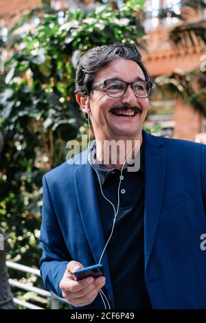 Aged businessman using smartphone with headphones and smiling Stock Photo