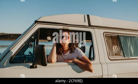 Pretty young brunette smiling and looking away while sitting inside vintage car on blurred background of nature Stock Photo