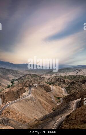 From above of narrow serpentine route in powerful brown mountains under cloudy colorful blue sky Stock Photo