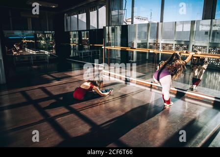 Young ballerinas working out in spacious sunny studio warming up muscles in front of mirror. Stock Photo