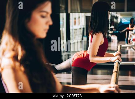 Side view of women practicing ballet with barre in sunny studio. Stock Photo