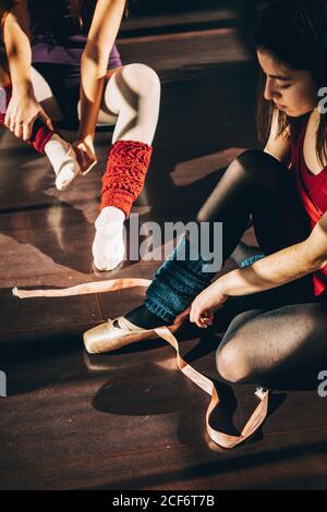 Young ballerinas wearing and lacing white pointe shoes in studio. Stock Photo