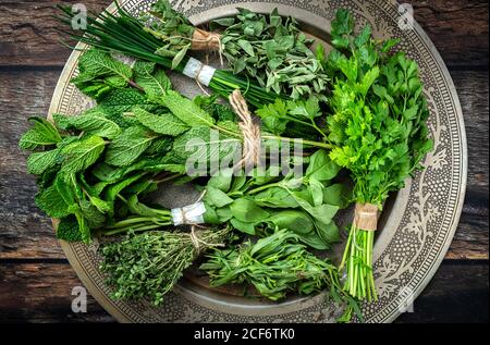 Top view of round plate filled with various fresh green aromatic herbs placed on wooden table