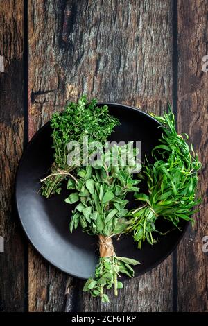 Top view of round plate filled with various fresh green aromatic herbs placed on wooden table