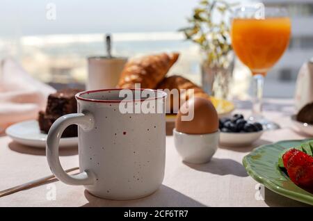 Homemade full brunch breakfast in sunlight with cooked eggs, blueberries, sponge cake, croissants, toast, tea, coffee and orange juice Stock Photo