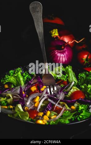 Healthy vegan food with fresh lettuce, cherries tomatoes, red onion and corn on dark background Stock Photo