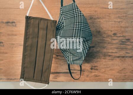 Stylish men face masks hanging in home closet. Different styles for fall outfits, brown fabric pleated and houndstooth plaid pattern mask Stock Photo