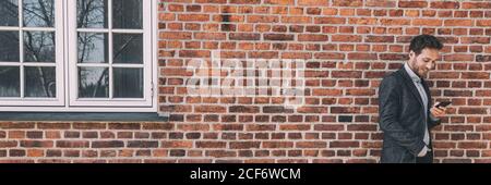 Happy business young man using mobile cellphone against city home brick wall background banner panorama Stock Photo