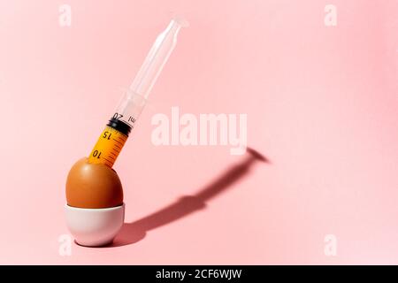 Cooking egg in eggcup with syringe taking out yellow raw yolk on pink background Stock Photo