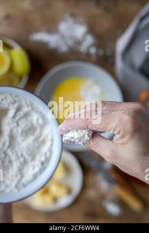 Top view of cropped unrecognizable female pouring wheat flour into bowl while preparing pastry at home Stock Photo