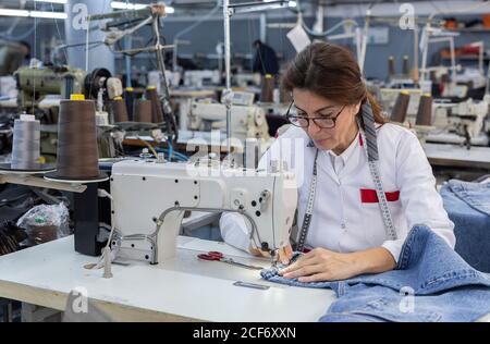 Working Woman hands in textile factory sewing on industrial sewing machine. Industrial production Stock Photo
