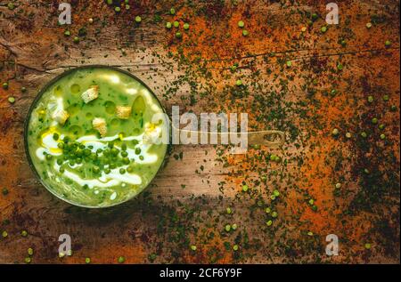 From above mashed vegetable creamy soup with small crackers and green peas on pan on wooden background Stock Photo