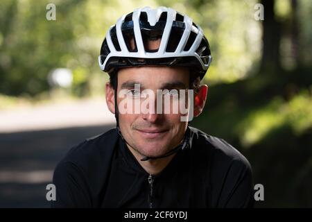 Confident adult man in bike helmet smiling and looking at camera on blurred background of park during training Stock Photo