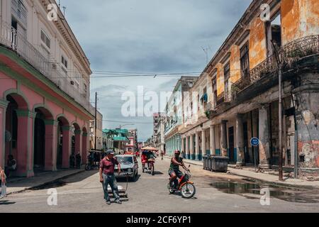 Havana, Cuba - DECEMBER 14, 2019: Typical city street with old colonial building and dilapidated house and road with various types of transport Stock Photo