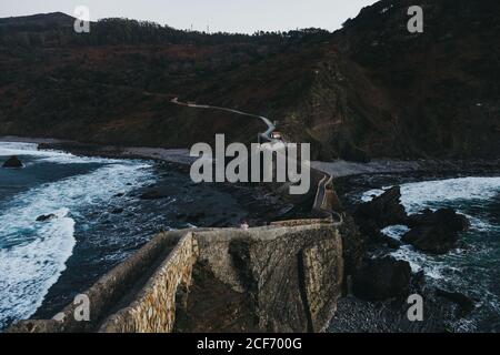 Winding mountain road crossing stone bridge and leading along rocky coastline in Spain at twilight Stock Photo