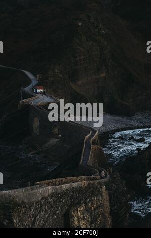 Winding mountain road crossing stone bridge and leading along rocky coastline in Spain at twilight Stock Photo