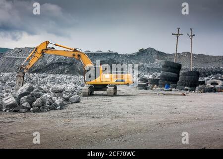 Heavy excavator with shovel standing on hill with rocks Stock Photo