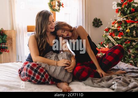 Two women friends relaxing in winter holidays at home near christmas tree in cozy interior. Interior with christmas decorations. Stock Photo